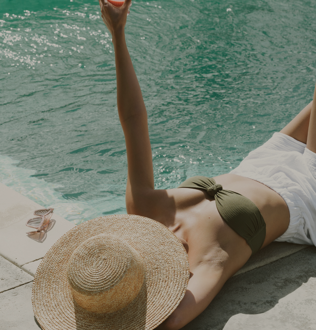 coaching transition de vie Bordeaux Femme allongée au bord de la piscine, portant un bikini et un chapeau de paille.